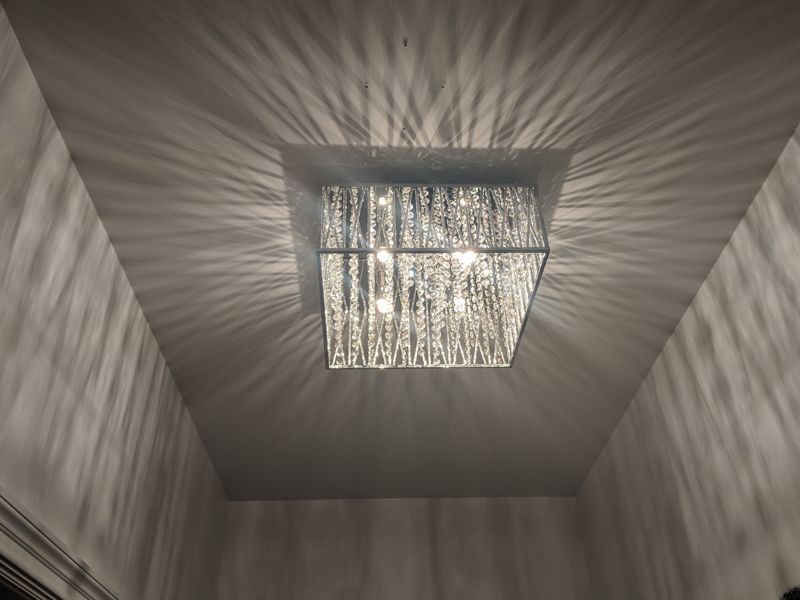 Ceiling light fixture casting starburst shadows across a small gray room