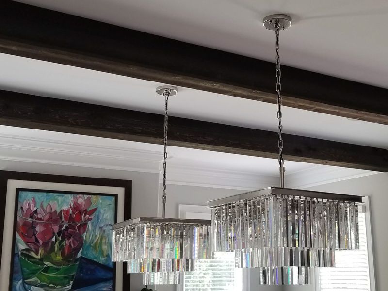 Modern dining room with two crystal pendant lights, dark ceiling beams, and a floral painting on the wall