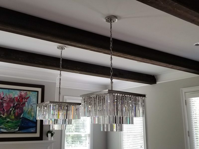 Dining room with two crystal pendant lights, dark ceiling beams, and a framed colorful painting on the wall