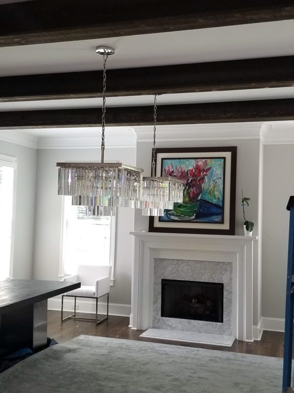 Living room with a fireplace, chandelier, dark ceiling beams, and a colorful painting above the mantel