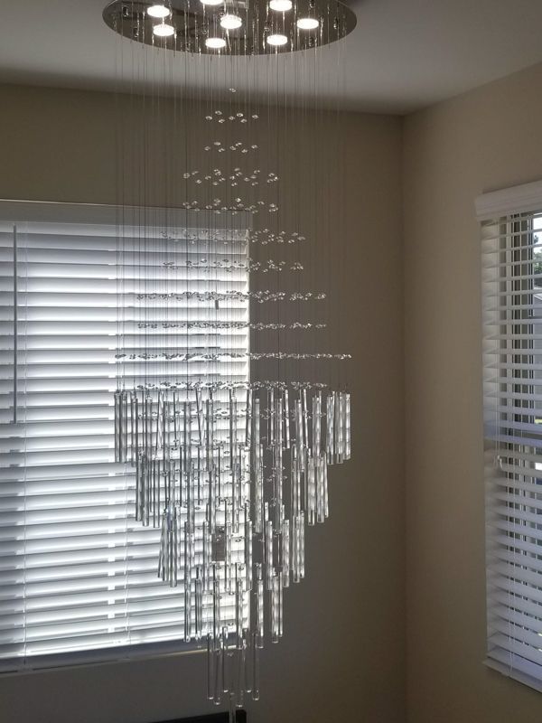 Crystal chandelier hanging in a beige room between two windows with white blinds