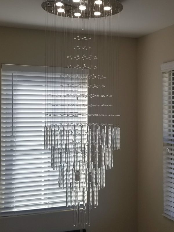 Modern chandelier of hanging crystal strands in a room with windows and white blinds