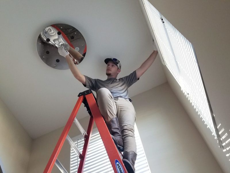 Person on a red ladder adjusting a ceiling fixture beside a window blinds panel