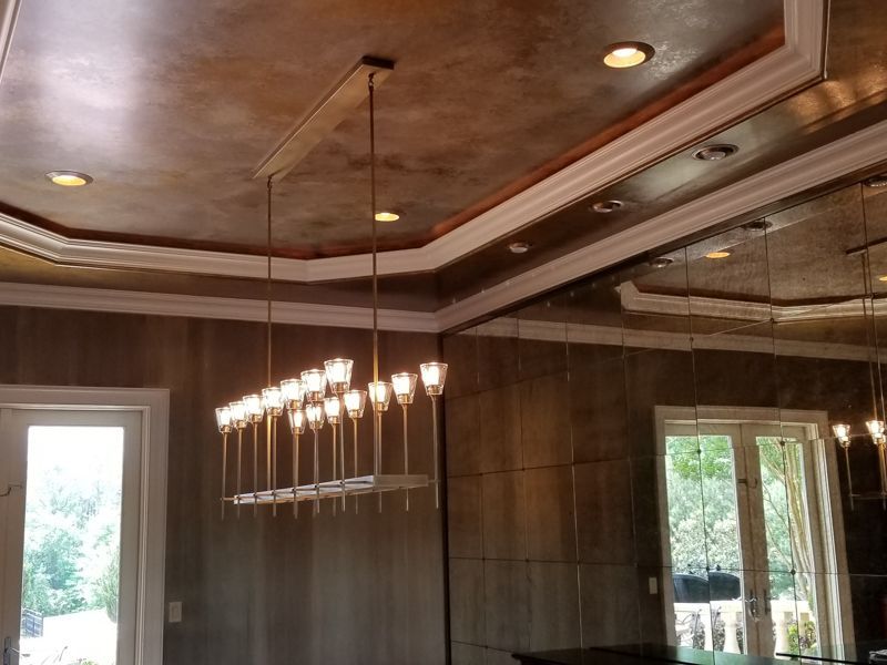 Elegant room with a chandelier, mirrored wall, and tray ceiling with recessed lights.