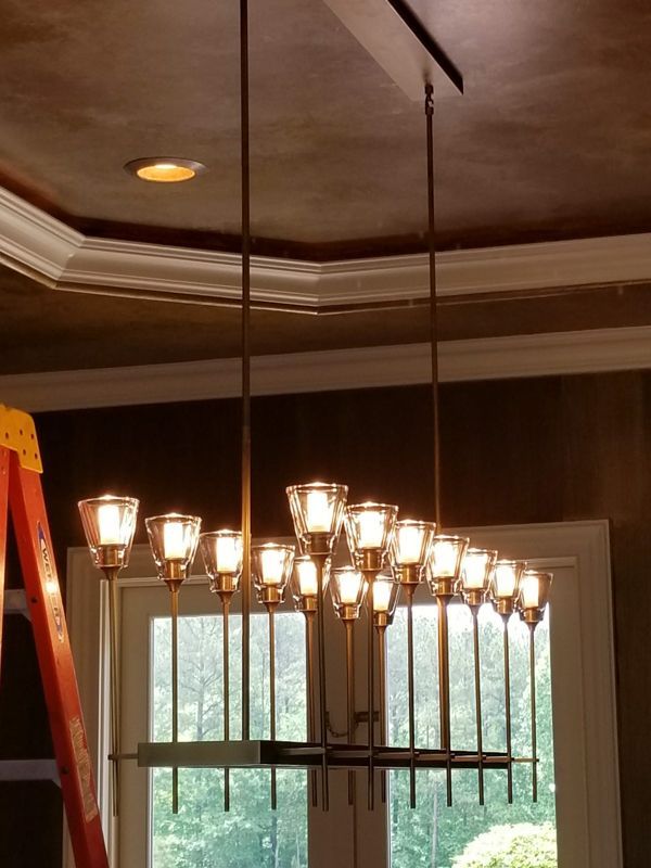 Ornate chandelier hanging from a dark ceiling in a room with crown molding and a window