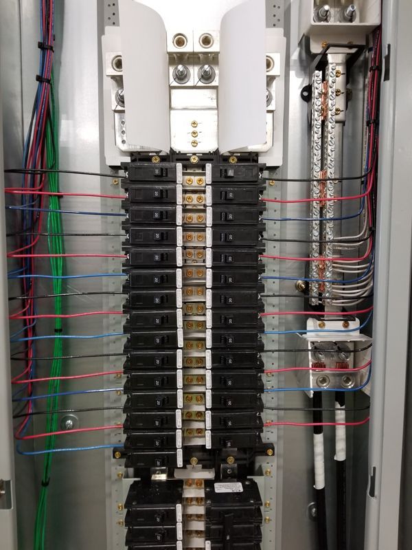 Open electrical panel with rows of circuit breakers and multicolored wires.