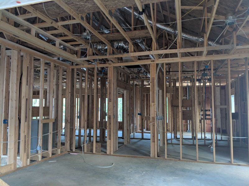 Unfinished house interior with exposed wooden framing, open walls, and bare concrete floor