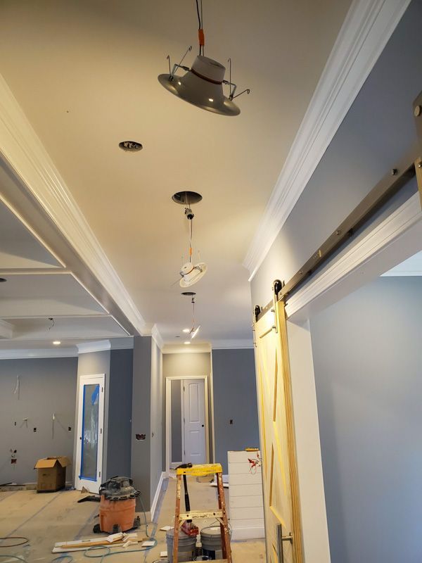 Interior hallway under construction with gray walls, white trim, exposed lights, and painting supplies.