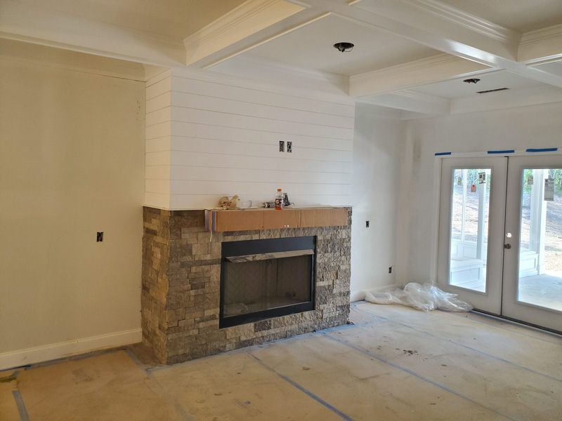 Unfinished living room with stone fireplace, white walls, and French doors to the outside.