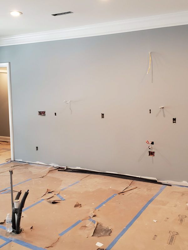 Partially renovated room with gray walls, exposed outlets, and taped cardboard covering the floor