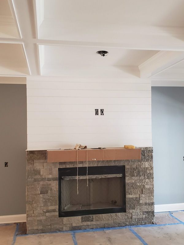 Living room fireplace with white shiplap wall, stone surround, and unfinished mantel shelf