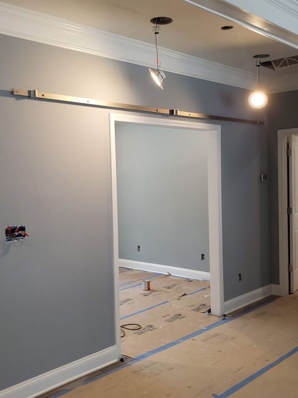 Interior room with gray walls, white trim, and a large doorway under construction, floor protected by plastic and tape