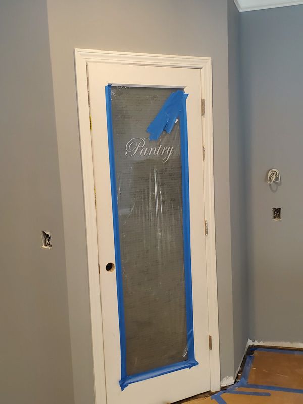 Doorway covered with taped plastic, blue painter’s tape, in a gray room under renovation