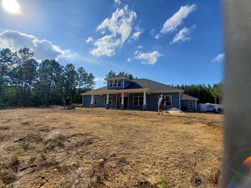 Single-story house under construction on a cleared lot beneath a bright blue sky