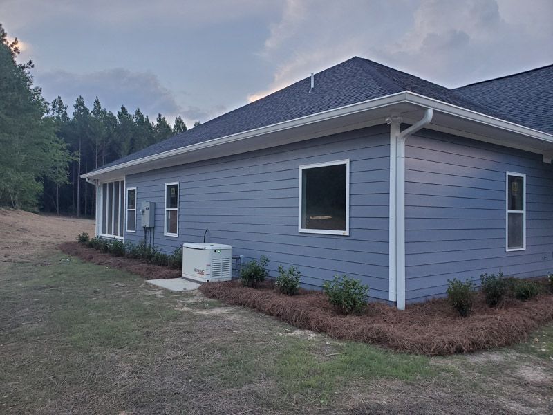 Side view of a gray house with a dark roof, white trim, and a small lawn at dusk.