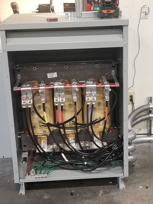 Open electrical cabinet with wiring, breakers, and exposed components in a workshop setting