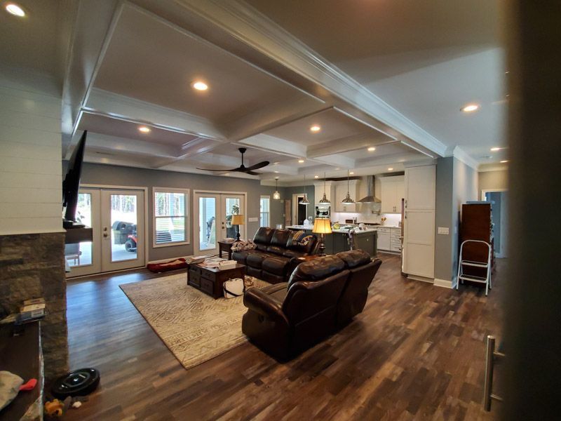 Spacious living room with leather sofas, hardwood floors, ceiling fan, and large windows overlooking a bright interior.