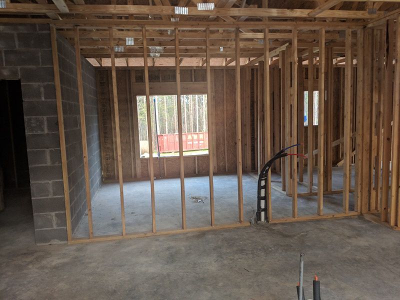 Unfinished room under construction with exposed wooden framing and a concrete floor, light coming through a window.