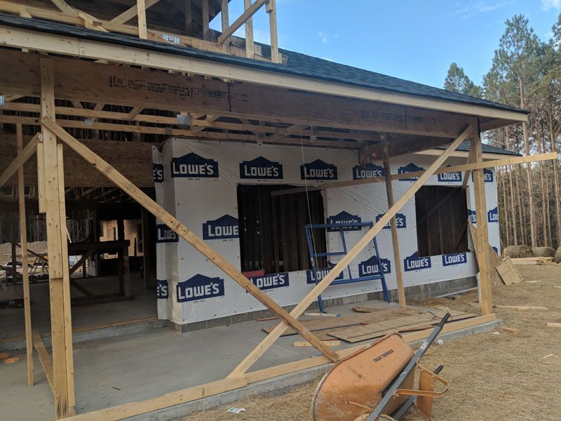 Unfinished house under construction with exposed framing, House wrap, and a wheelbarrow in front.
