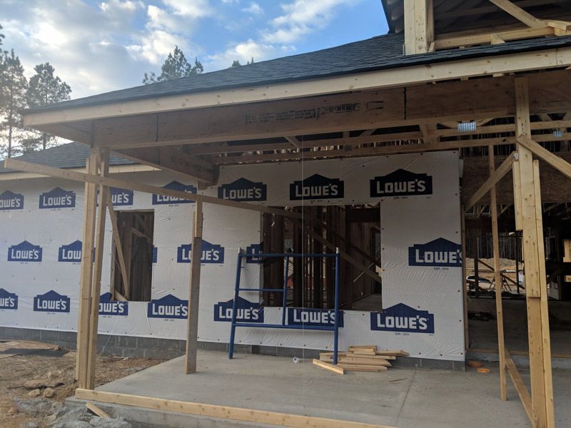 Partially built house framed in wood with Lowe’s house wrap and an unfinished porch