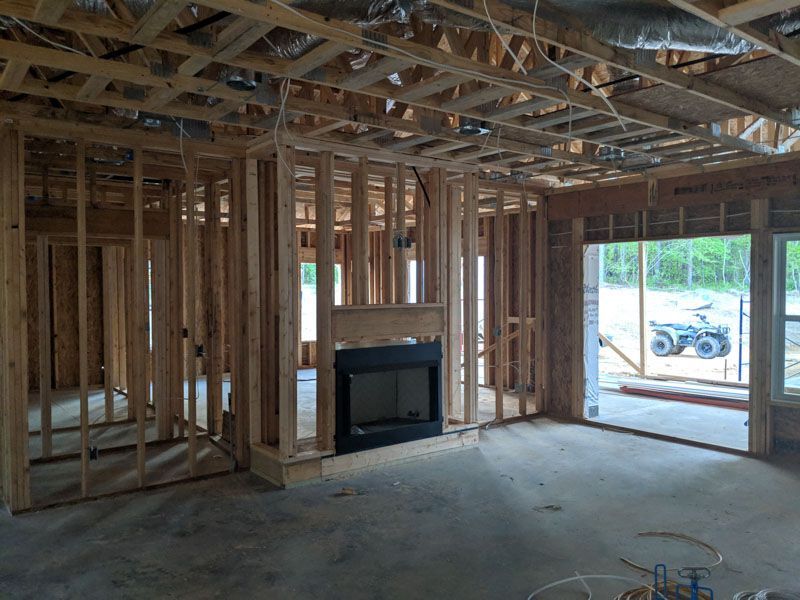 Unfinished house interior with exposed framing, a fireplace, and large windows/doorways letting in daylight.