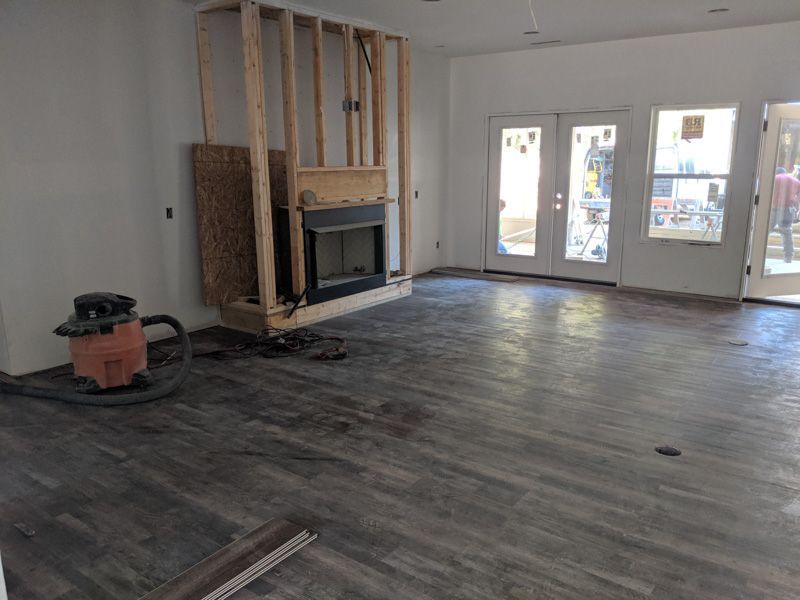 Empty living room under renovation with exposed wall framing, fireplace, and dark wood flooring.