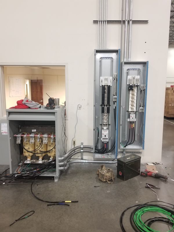 Electrical panels and conduit in a utility room, with tools and cables on the floor.
