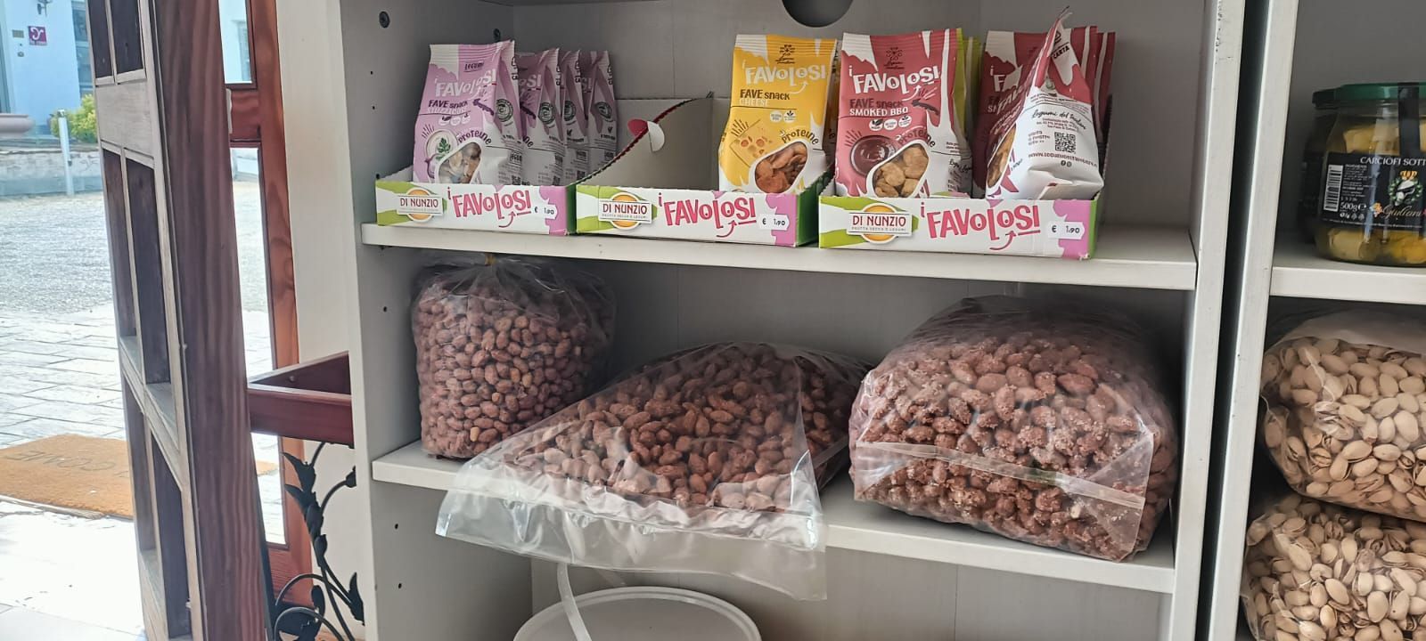 Scaffali pieni di snack confezionati e arachidi sfuse in una piccola bancarella del mercato.