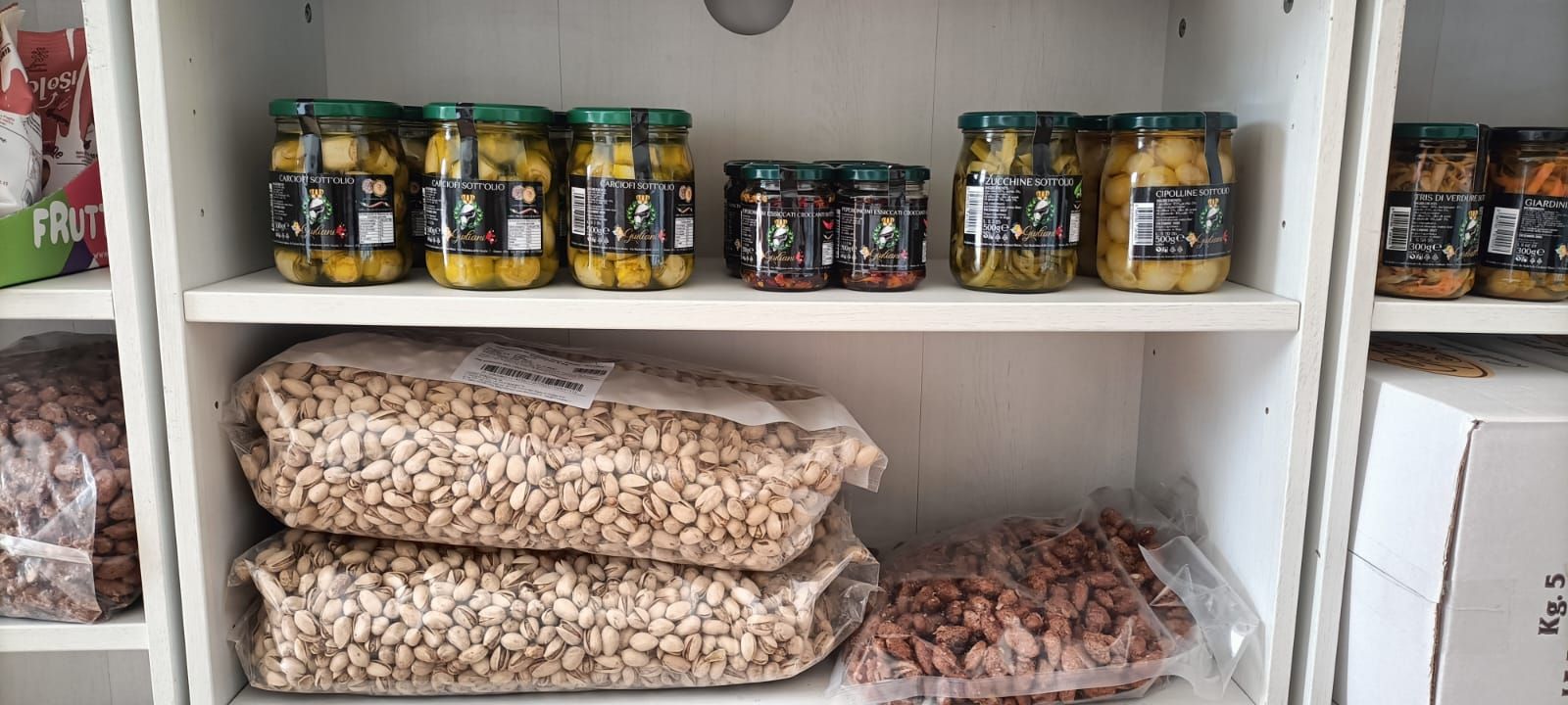 Dispensa con scaffali, barattoli di conserve e sacchetti di frutta secca o legumi su ripiani bianchi.