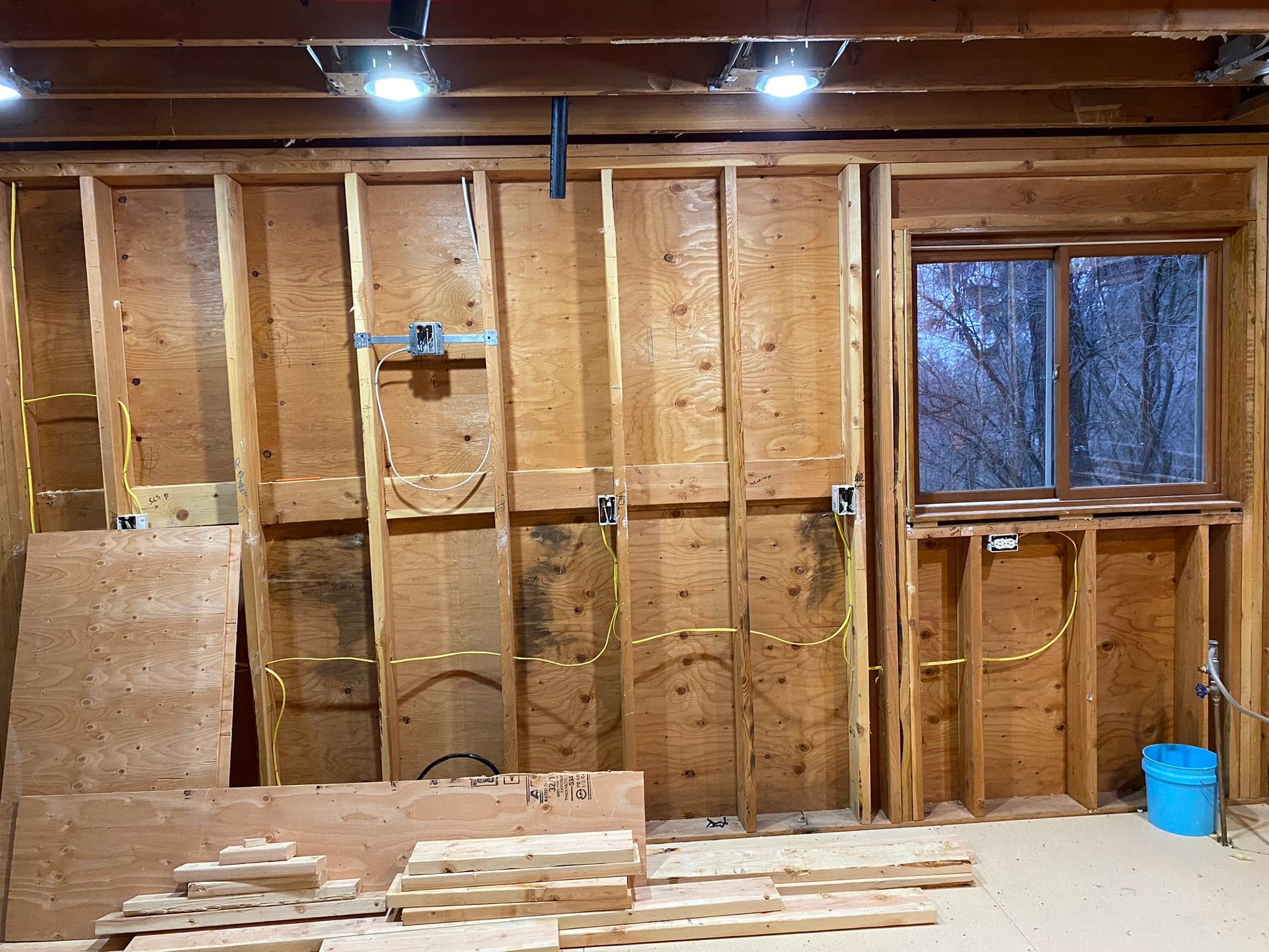 An unfinished interior wall with wooden studs, electrical wiring, and an installed window in a room under construction.
