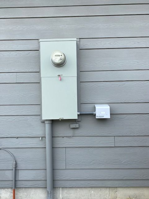 A gray electrical meter and a small junction box mounted on light gray horizontal siding.