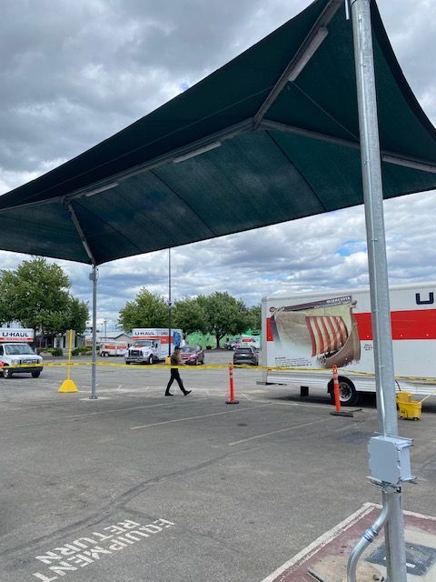 A U-Haul parking lot with a large green canopy covering equipment return spaces under a cloudy sky.