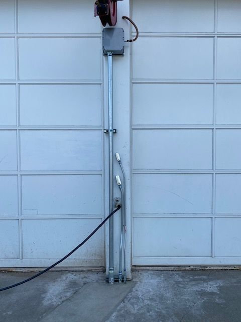 An electric vehicle charging station with a plug connected to a wall-mounted outlet, installed on a white garage door.