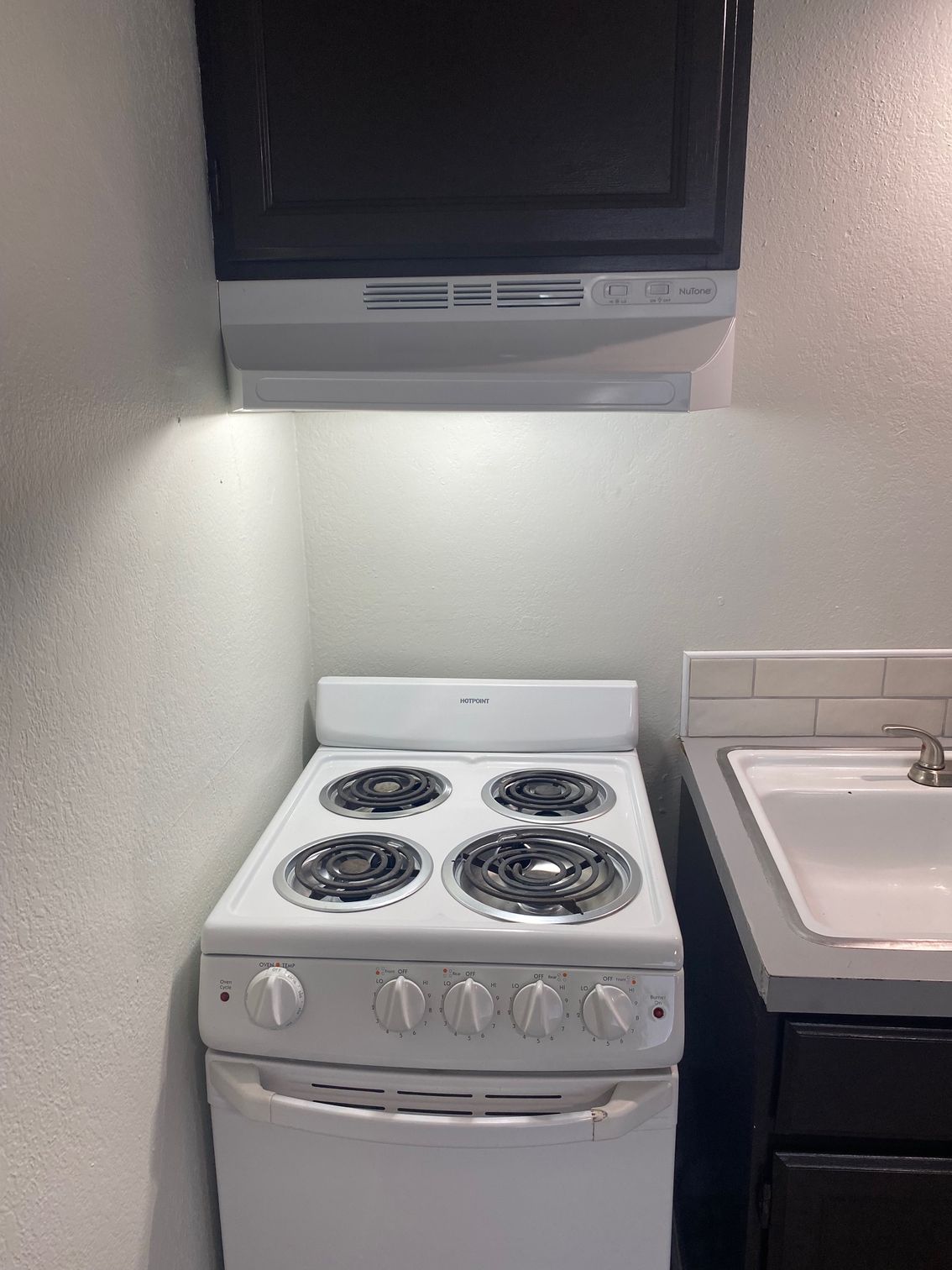 A white electric stove with four burners sits beneath a black microwave range hood in a kitchen next to a sink.