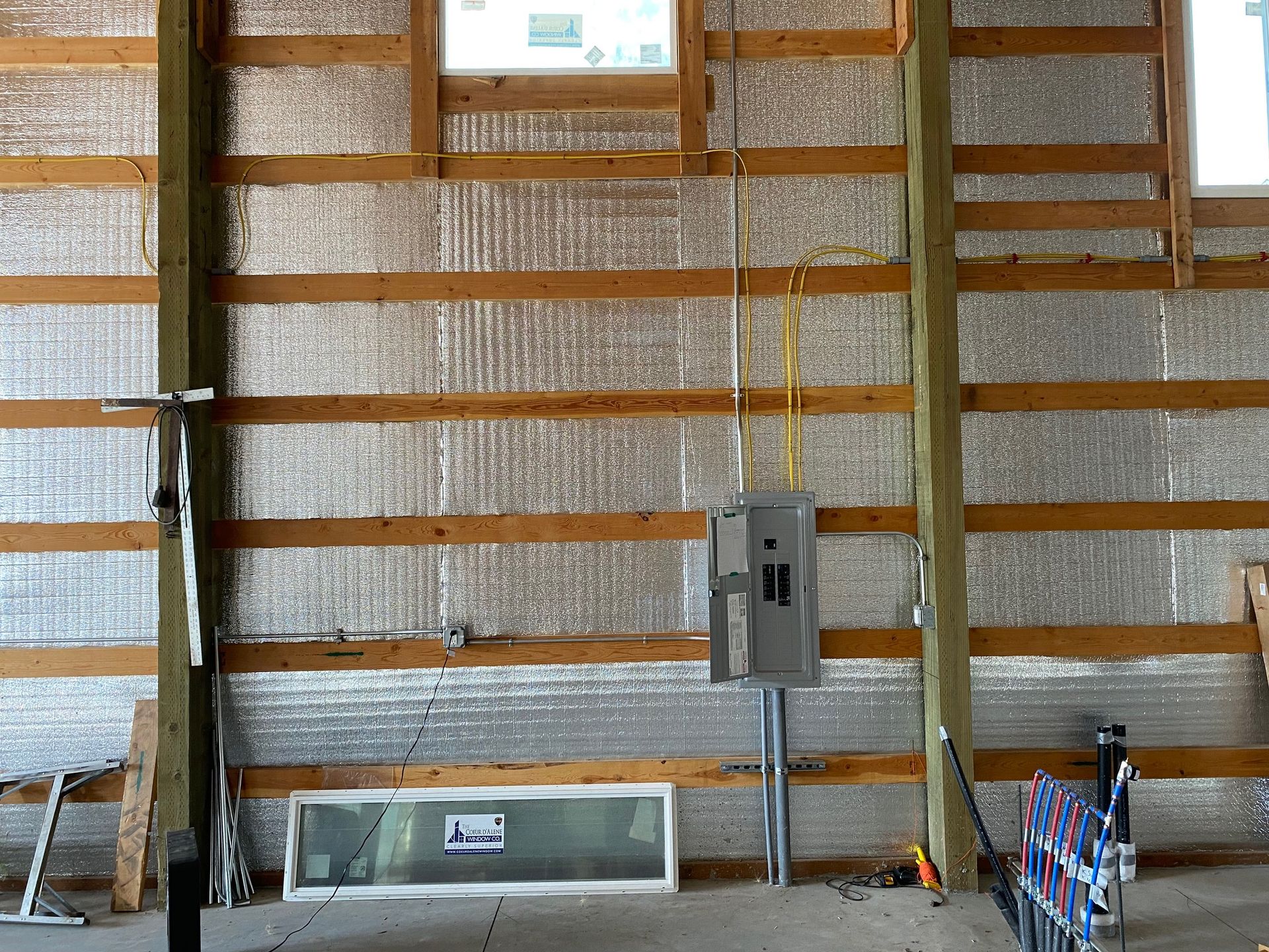 Electrical panel on an unfinished wall with horizontal wood framing and metallic insulation inside a building.