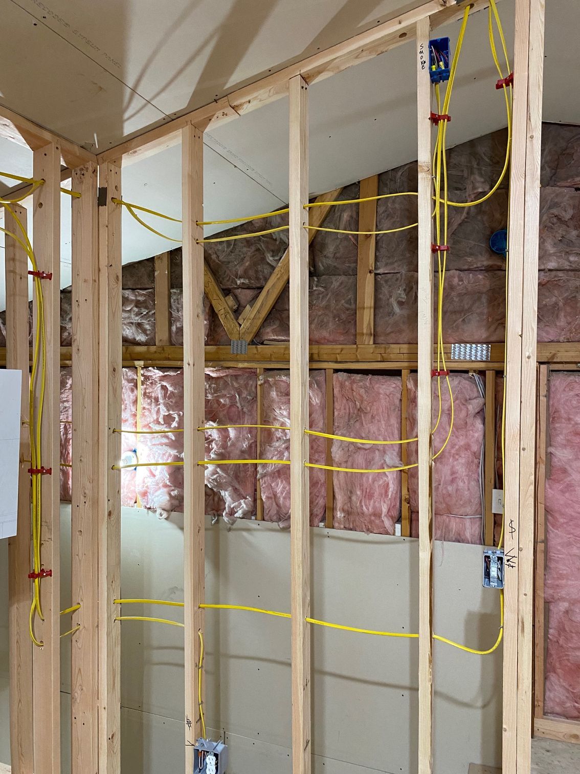 Framing of a residential wall showing yellow electrical wiring running through wooden studs and blue outlet boxes.