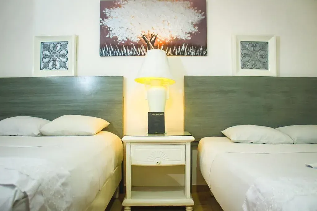 Two beds in a hotel room, a nightstand with a lamp between them, art above.