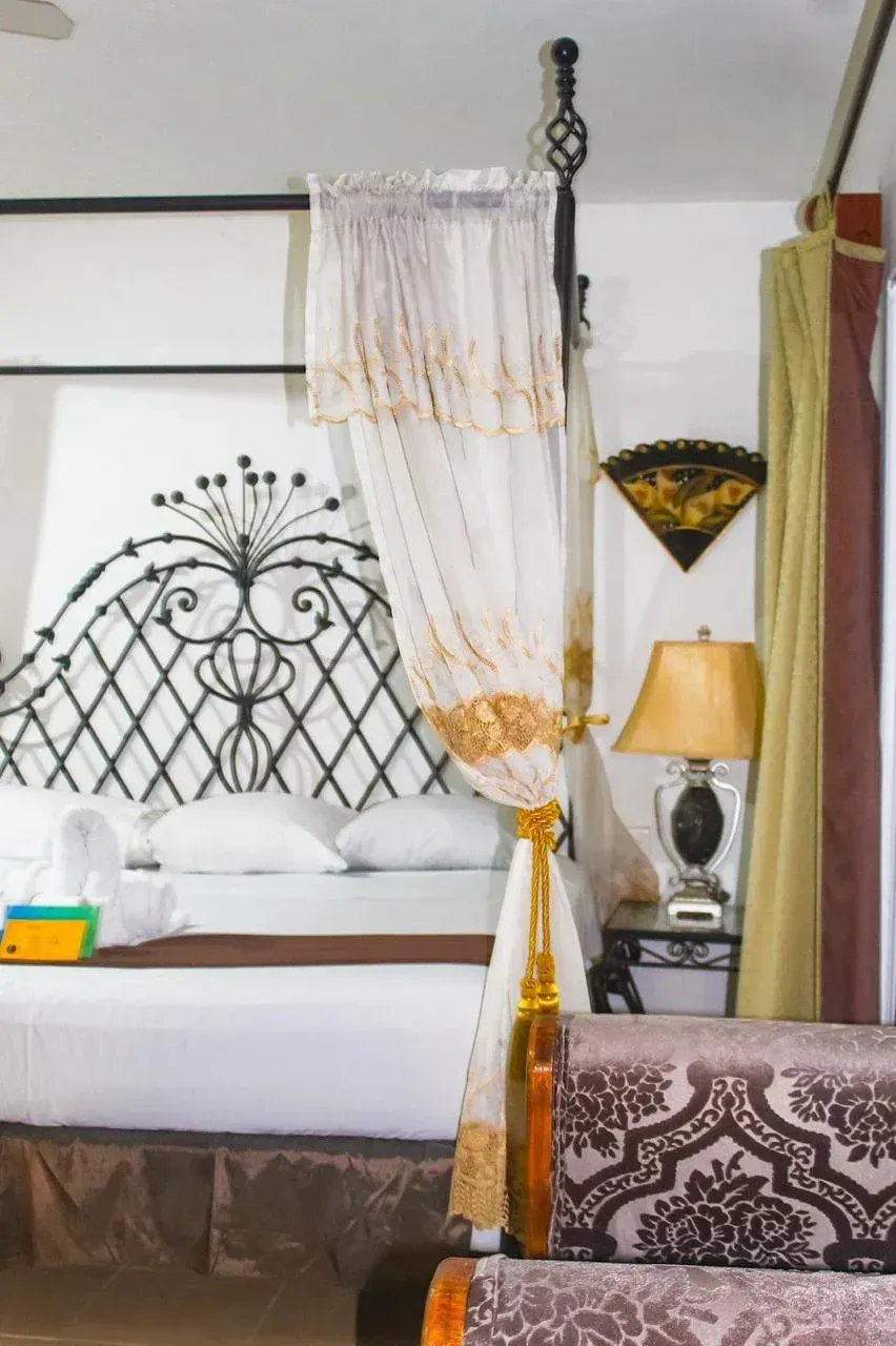Bedroom with ornate black headboard, canopy bed, sheer curtains, and side table with lamp.