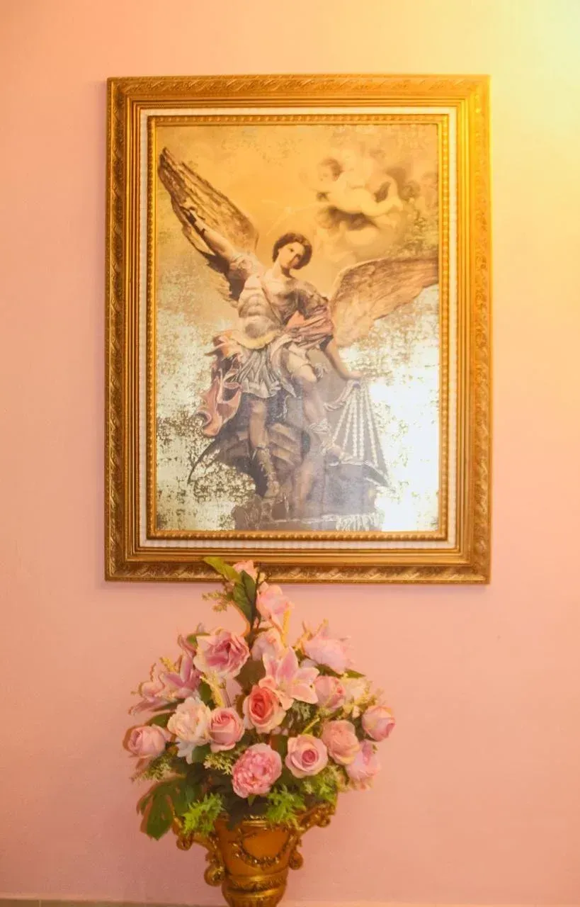 Painting of an angel with gold frame, above a vase of pink flowers on a pink wall.