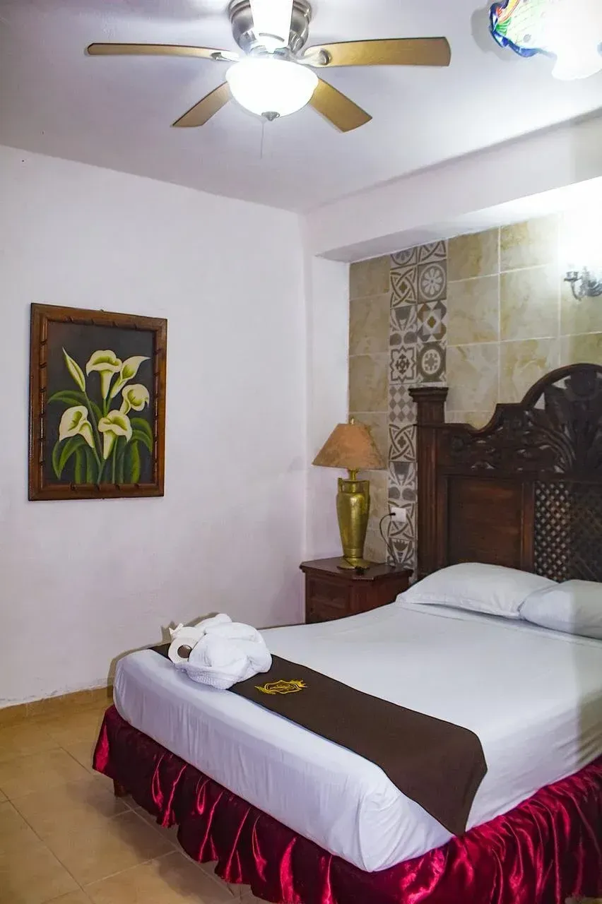 Bedroom with wooden bed, brown and white bedding, art, and a ceiling fan.