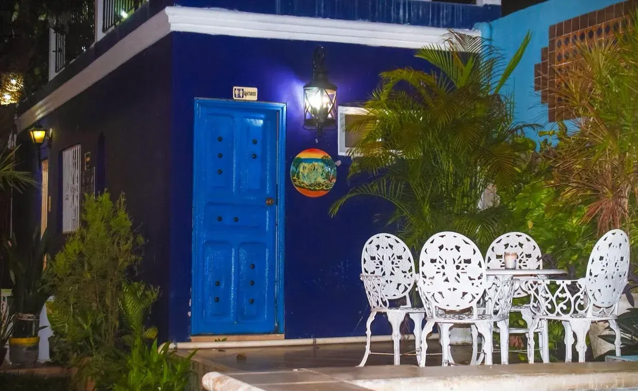 Blue building with ornate blue door, white patio furniture, and lush greenery.