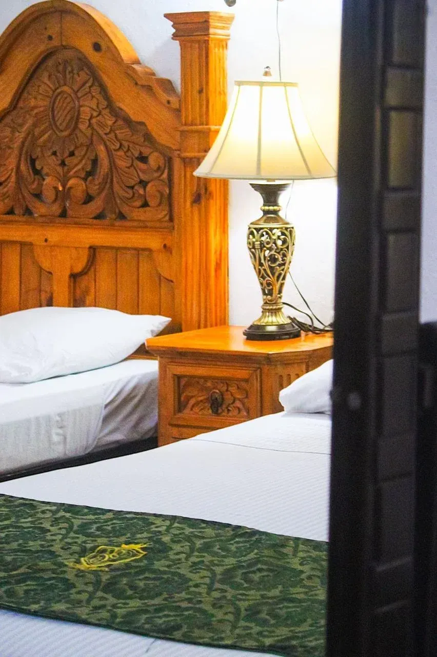 Two twin beds with wooden carved headboard, bedside table with lamp.