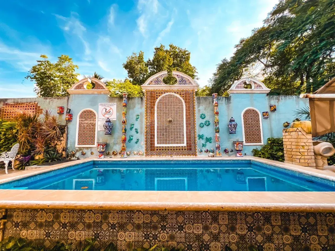 Swimming pool with ornate blue wall backdrop and decorative arches. Sunny day.