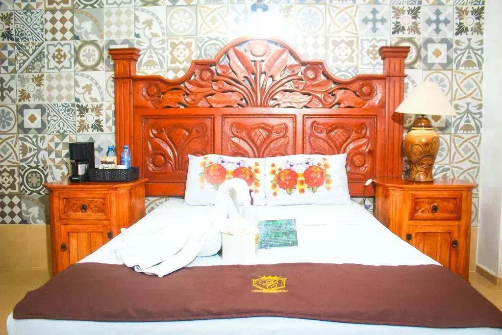 Bedroom with a carved wooden headboard, nightstands, a double bed with decorative pillows, and a patterned tile wall.