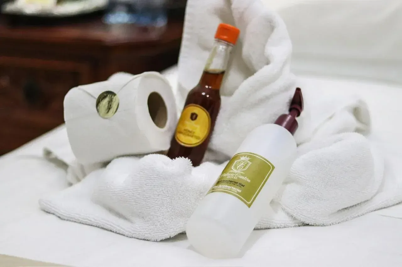White towels, toiletries (liquid soap, oil, toilet paper) arranged on a bed.