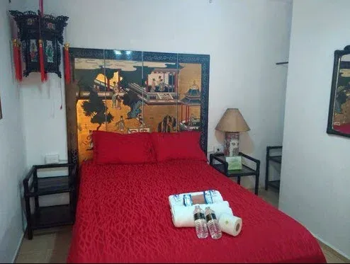 Dormitorio de temática roja con cabecero decorativo, mesita de noche y farol. La cama tiene toallas, botellas.