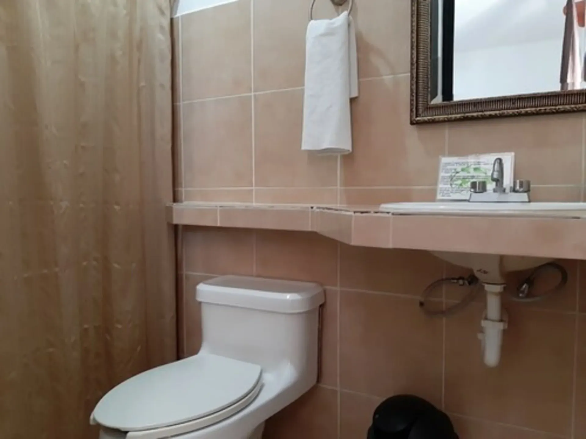 Baño con inodoro, lavabo, espejo y azulejos beige. Hay una toalla colgada en la pared.