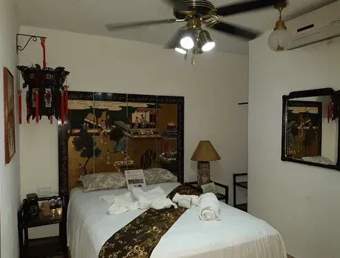 Dormitorio con cama, cabecero artístico, ventilador de techo y linterna decorativa.