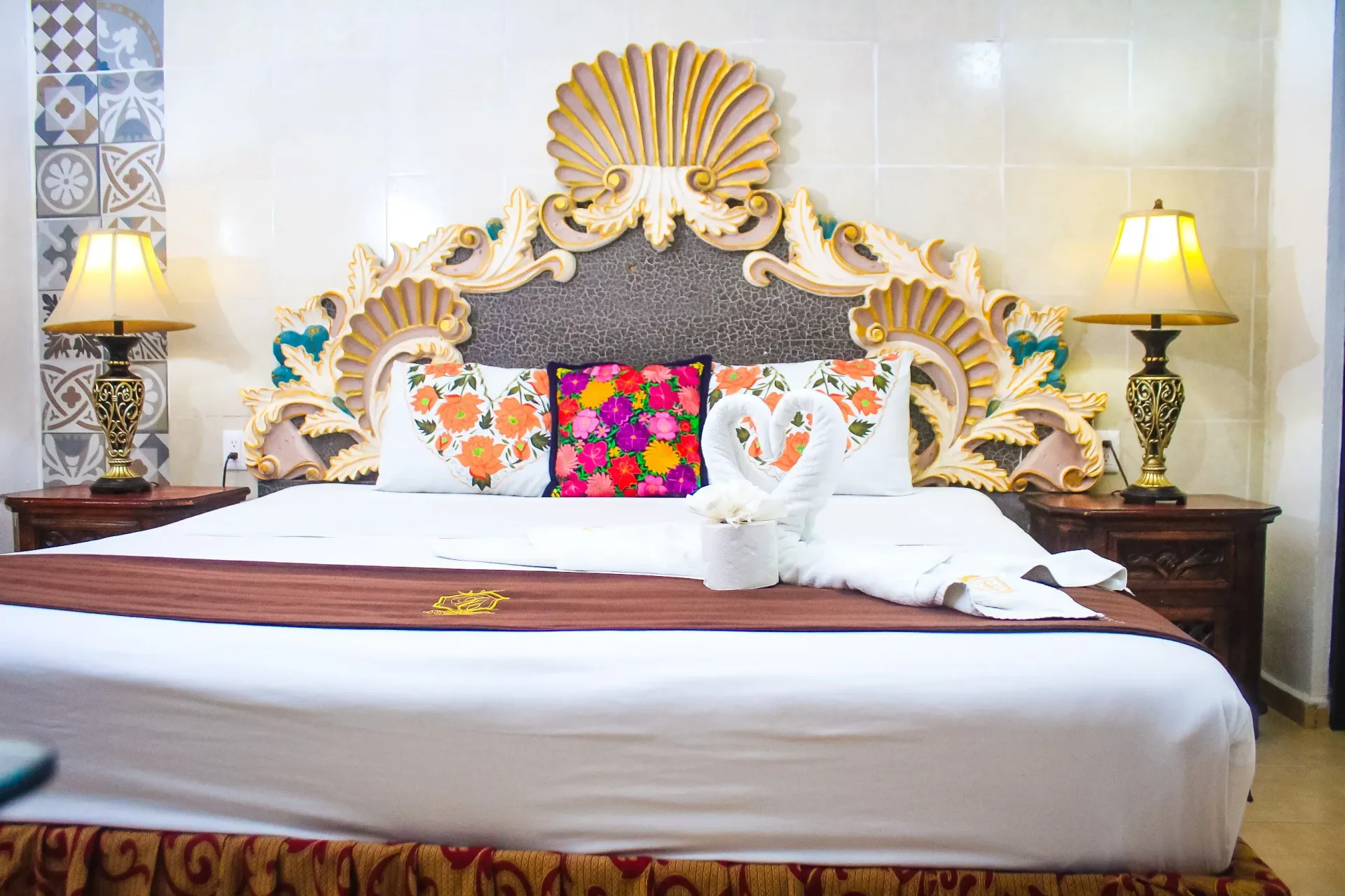 Habitación de hotel adornada con una cama grande, cabecera decorativa y lámparas de noche.