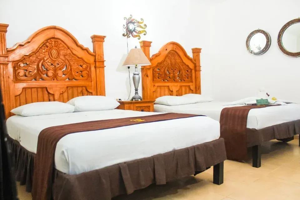 Dormitorio con dos camas con cabeceros de madera ornamentados, una lámpara de noche y dos espejos redondos.
